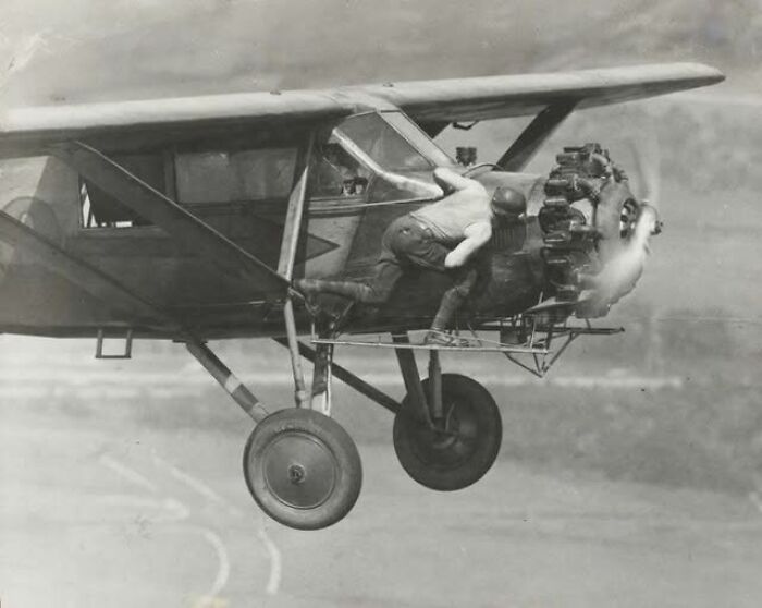Man leaning out of vintage airplane engine during flight in an antique historical photograph showing early aviation technology.
