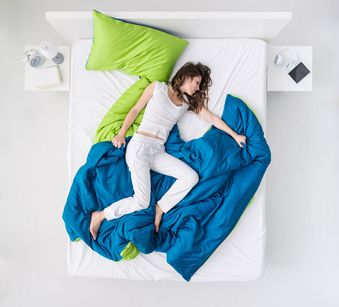Woman lying alone on bed with blue and green blankets, representing why women love being alone and enjoy solitude.