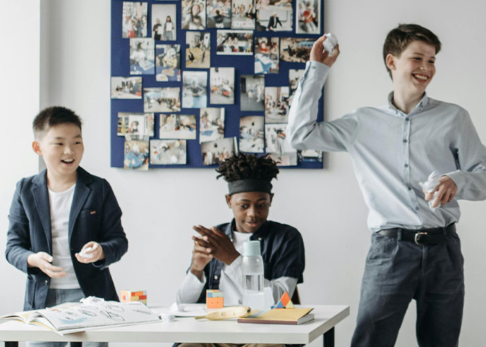 Three boys having fun in a classroom, showing a memorable take one for the team moment together.