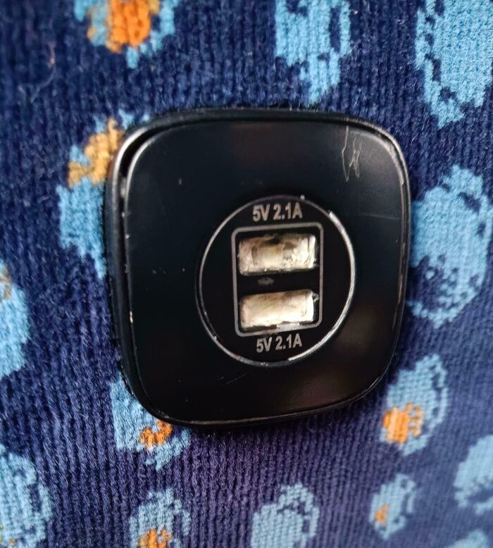 Close-up of a damaged USB charging port on patterned fabric, highlighting issues faced by public transport passengers.